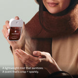 Woman in brown sweater holding Touchland Power Mist hand sanitizer bottle