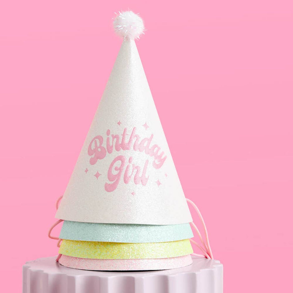 Pastel glitter birthday girl party hat with white cone and colorful paper bands on pink background