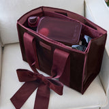 Red velvet tote bag with bow handles containing cosmetics and accessories
