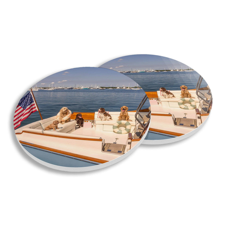 Ceramic coasters featuring dogs on a boat, displayed on a wooden vessel with water and sailboats in background