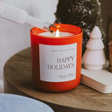 Happy Holidays soy candle by Sweet Water Decor displayed on wooden surface with festive decorations