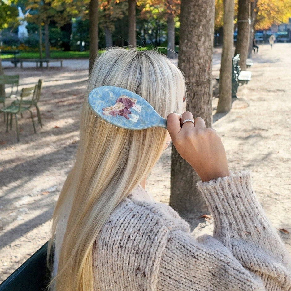 Hand-painted horse hair brush held by woman with blonde hair in outdoor park setting