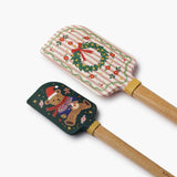 Two festive silicone spatulas with wooden handles featuring Christmas designs: wreath and teddy bear.