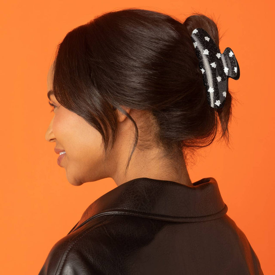 Black glitter ghost claw clip worn in updo hairstyle on model against orange background
