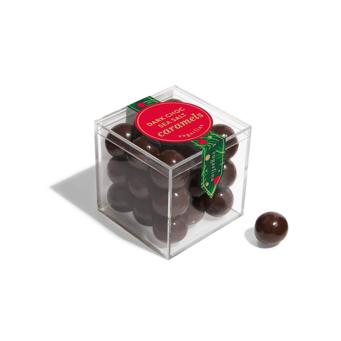 Sugarfina Dark Chocolate Sea Salt Caramels in clear cube box with red label and one piece displayed beside.