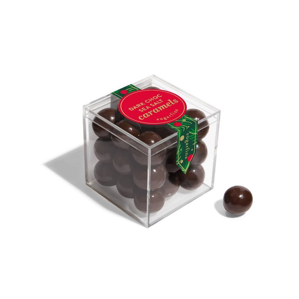 Sugarfina Dark Chocolate Sea Salt Caramels in clear cube box with red label and one piece displayed beside.