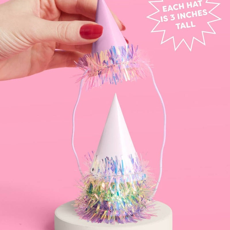Hand holding iridescent mini party hat with colorful foil fringe decoration on pink background