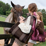 Girl holding espresso polka dot bow jelly tote bag while petting a horse in a rural setting.