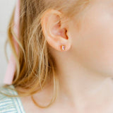 Pink gemstone screwback stud earrings worn by model with blonde hair in close-up