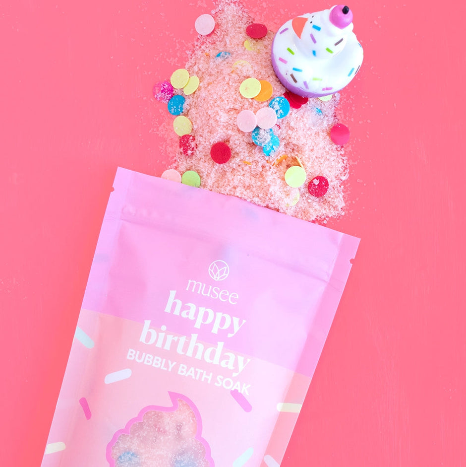 Musee happy birthday bath soak with colorful sprinkles on a pink background