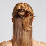 Person with long blonde hair styled in a bun using a tortoiseshell hair clip on a light gray background