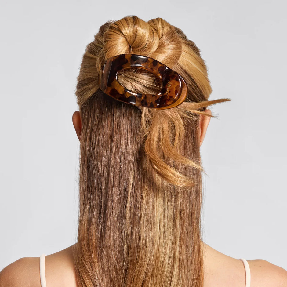 Person with long blonde hair styled in a bun using a tortoiseshell hair clip on a light gray background