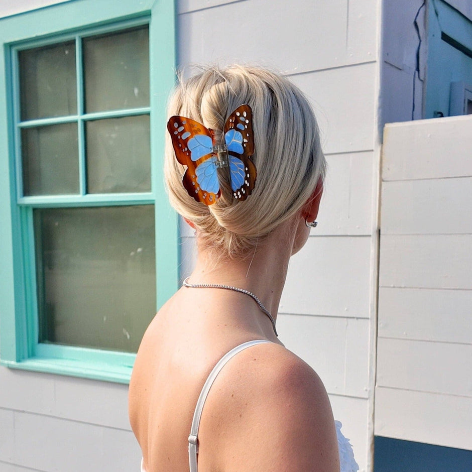 Hand-painted monarch butterfly claw hair clip worn in blonde updo hairstyle outdoors