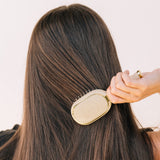 Woman using tan TELETIES Mini Detangler Brush on long brunette hair