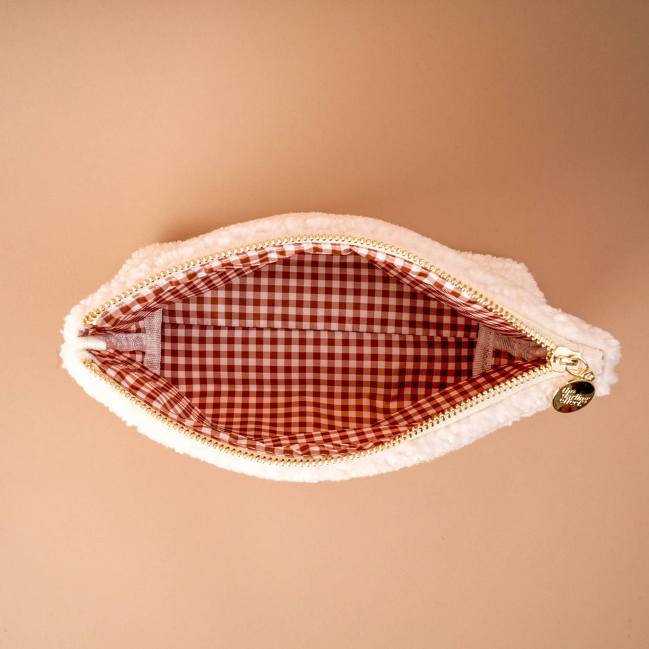 Cream teddy pouch with red gingham lining, gold zipper, and charm detail