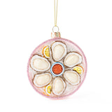 Pink glittered glass ornament featuring oysters, lemon slices, and cocktail sauce design
