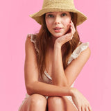 Woman wearing beige straw bucket hat and textured top against pink background