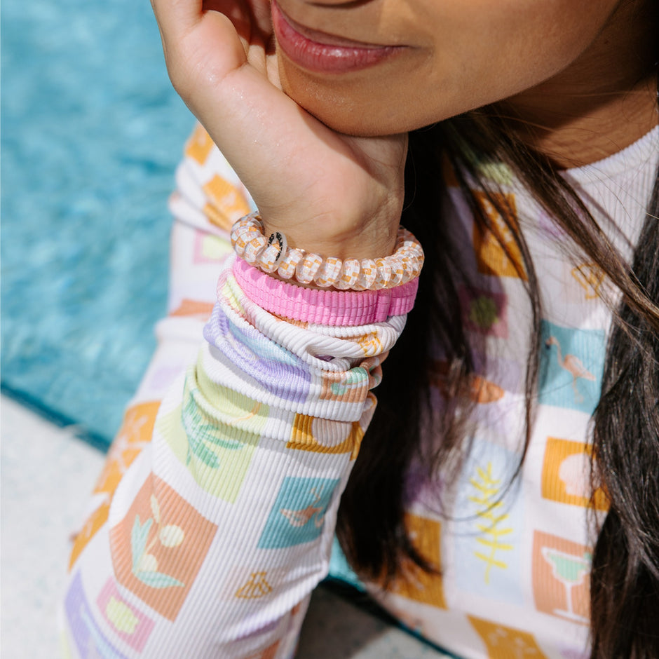 Woman wearing colorful Island Threads hair ties on wrist by pool in patterned cover-up