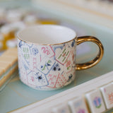 Mahjong tiles coffee mug with gold handle on light blue surface with stationery