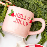 Pink Holly Jolly mug surrounded by evergreen branches and candy canes in festive holiday setting