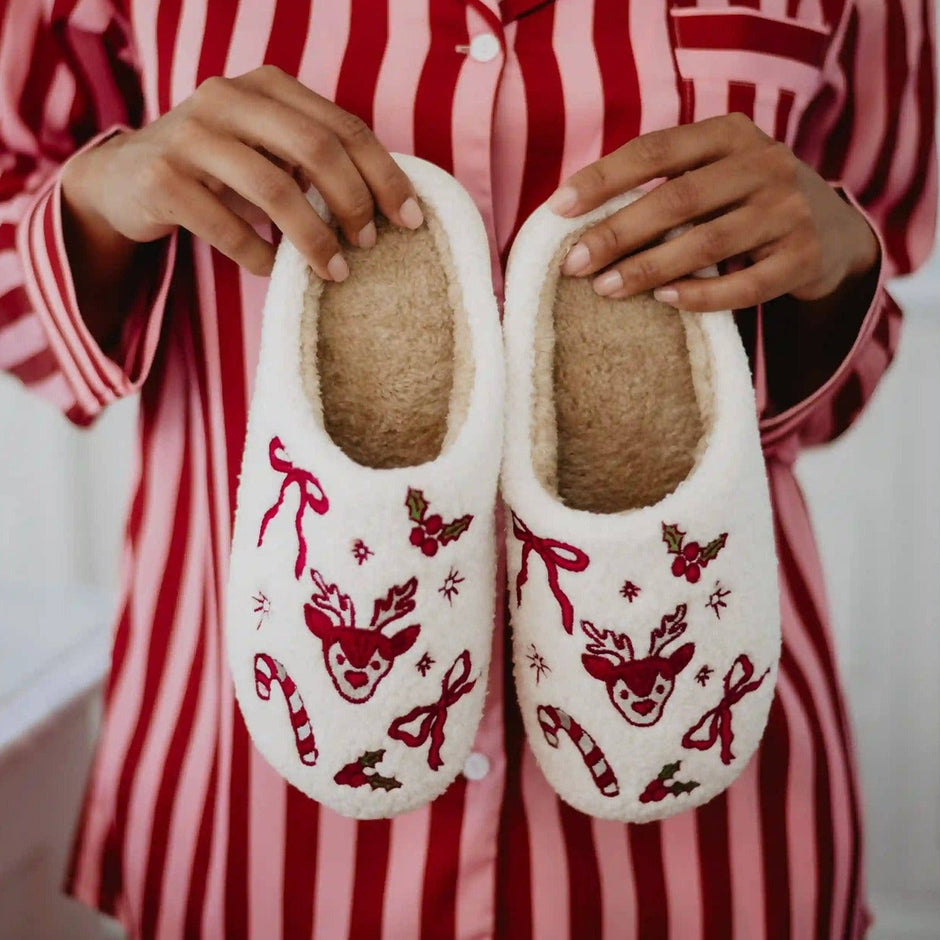 Woman wearing red striped pajamas holding Christmas reindeer slippers with bow details