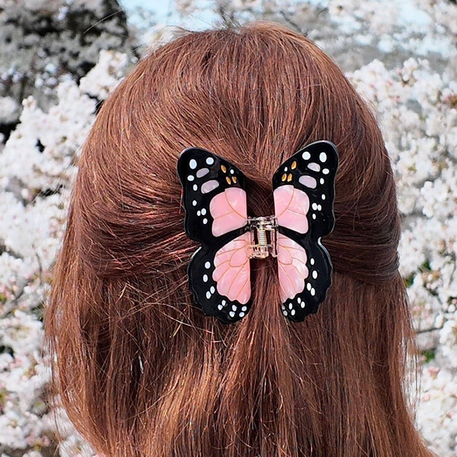 Hand-painted monarch butterfly claw clip worn in long brown hair against white flowering background