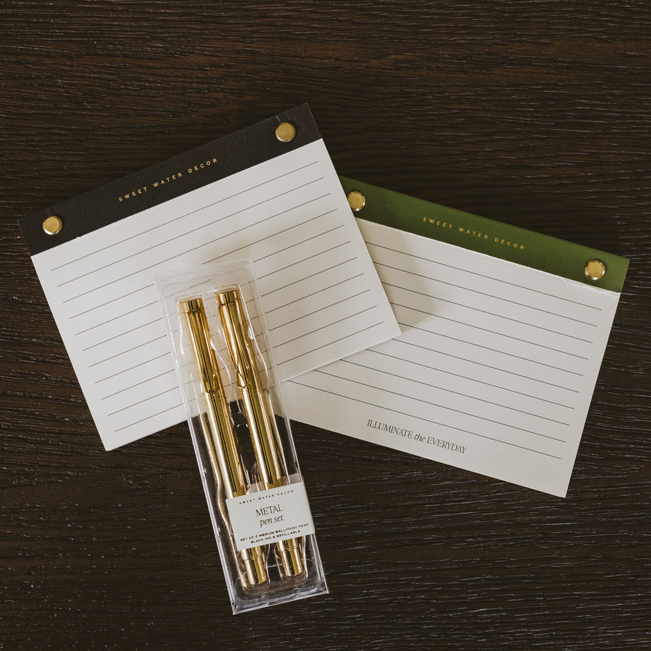 Gold metal pen set displayed with Sweet Water Decor lined notecards on dark wood surface