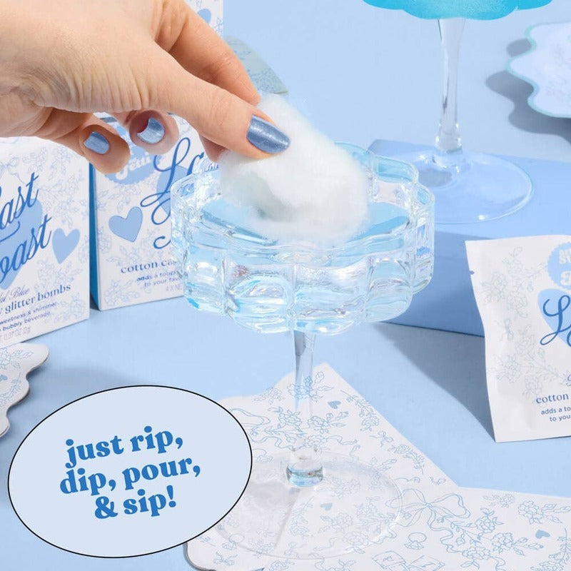 Hand holding cotton candy glitter bomb over champagne coupe glass in blue-themed bachelorette party setting