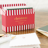 Red and white striped Christmas card box by Sugar Paper displayed on wooden desk with stationery.