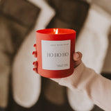 Ho Ho Ho red soy candle held in hands with festive holiday styling and neutral background