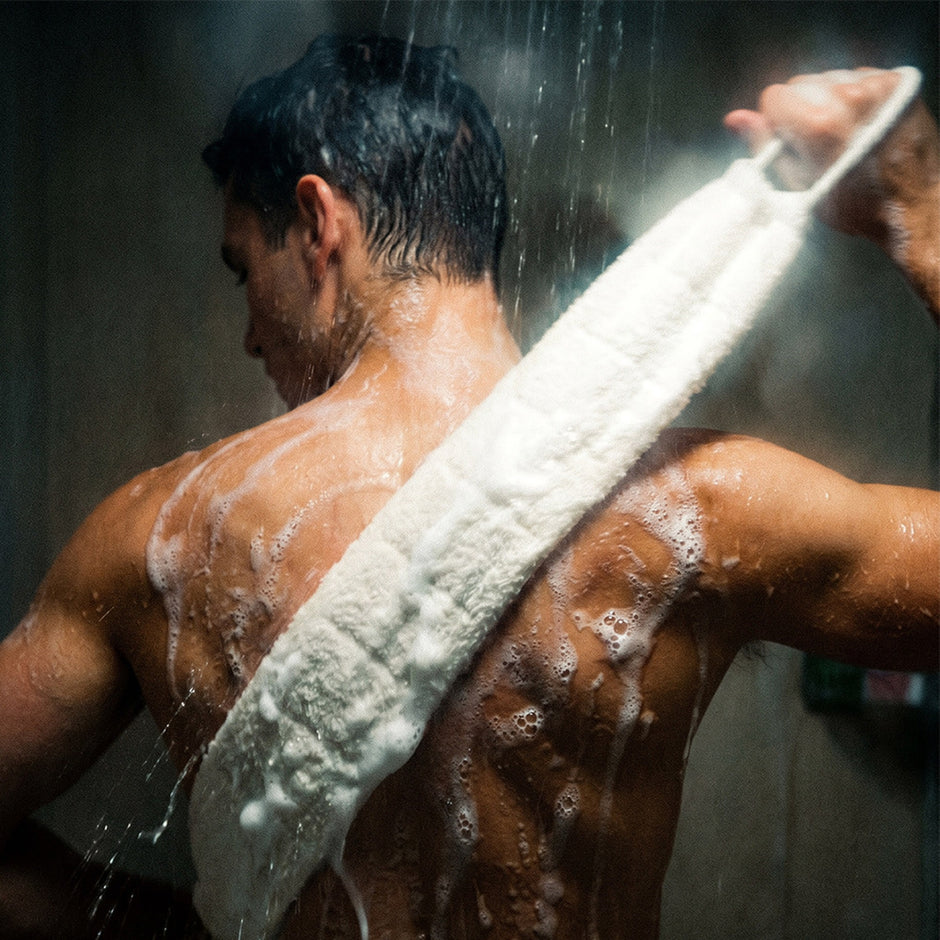 Man using SPONGELLÉ body wash infused back scrubber in shower with water streaming down