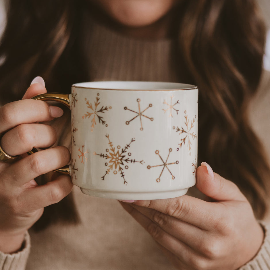 Gold snowflake coffee mug held by woman in cozy sweater, warm holiday beverage styling