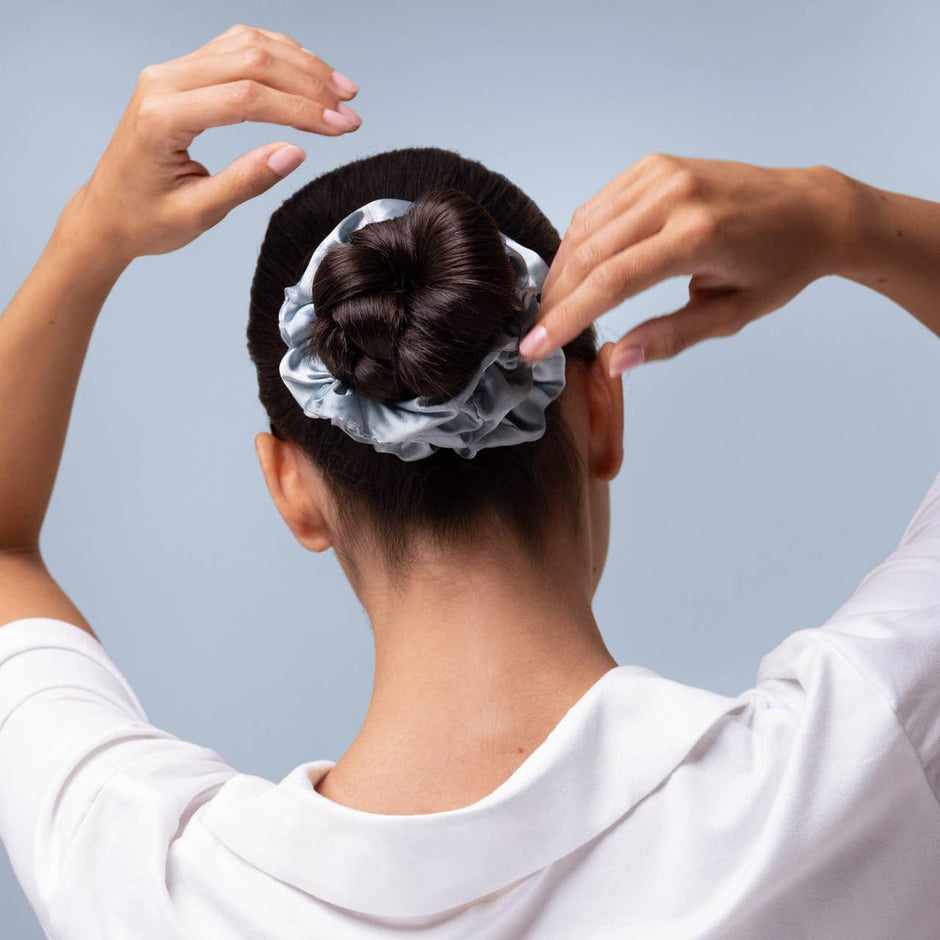 Woman wearing Kitsch satin sleep scrunchie in haze blue, styled in updo bun hairstyle