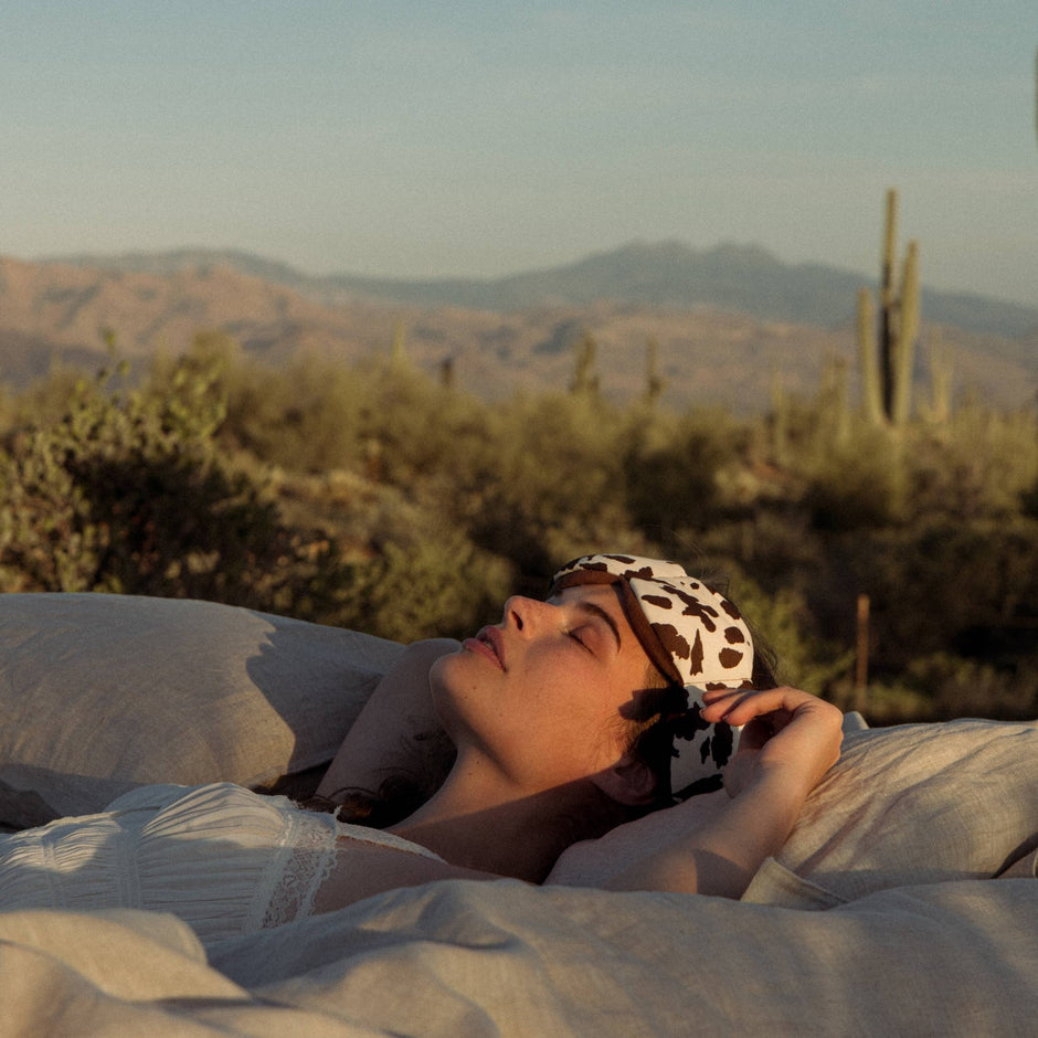 Person wearing cowhide weighted sleep mask while resting outdoors in desert landscape