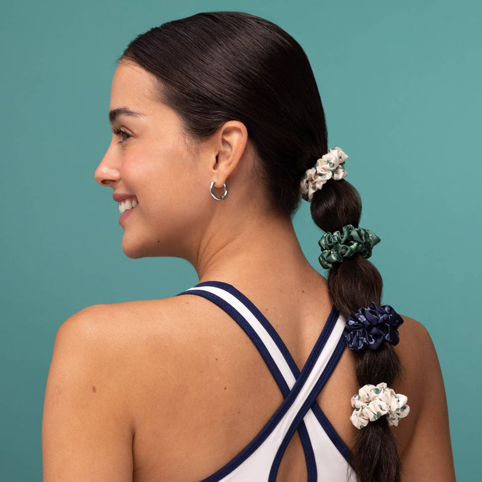 Woman wearing navy sports top with braided hair styled with cream, green, and navy satin scrunchies