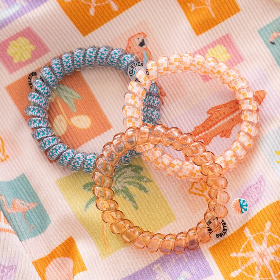 Three colorful TELETIES hair ties displayed on a patterned fabric background