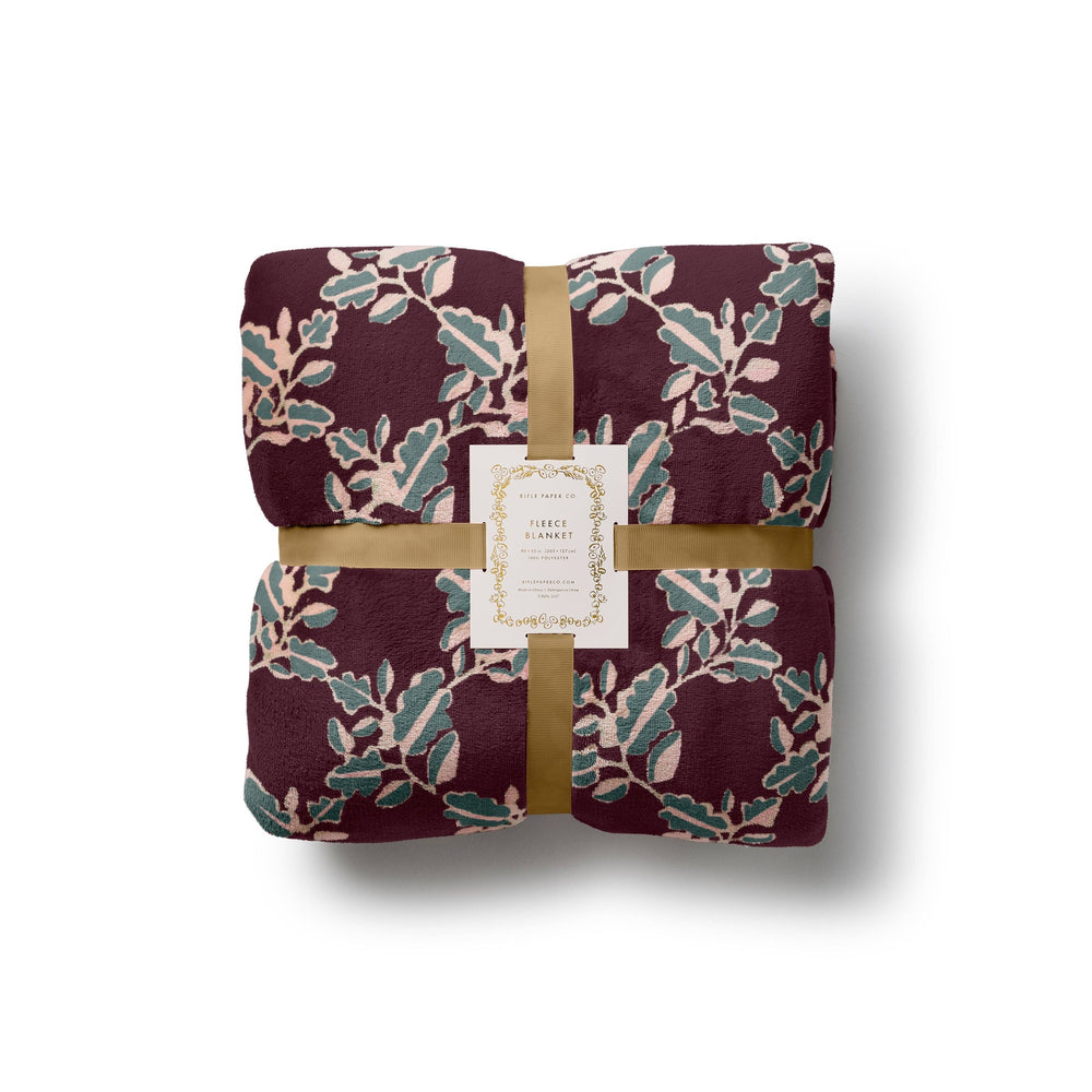 Rifle Paper Co. Portico Fleece Blanket in burgundy with botanical leaf pattern, wrapped with gold ribbon