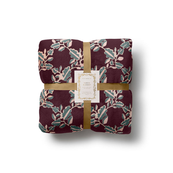 Rifle Paper Co. Portico Fleece Blanket in burgundy with botanical leaf pattern, wrapped with gold ribbon