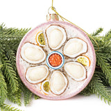 Pink glittered oyster ornament with shells and lemon slices displayed among evergreen branches
