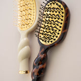 Tortoise shell vented hair brush with gold paddle and black bristles on neutral background
