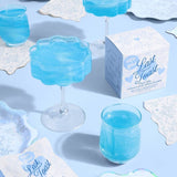 Last Toast cotton candy glitter bombs in blue cocktails with decorative napkins on white surface