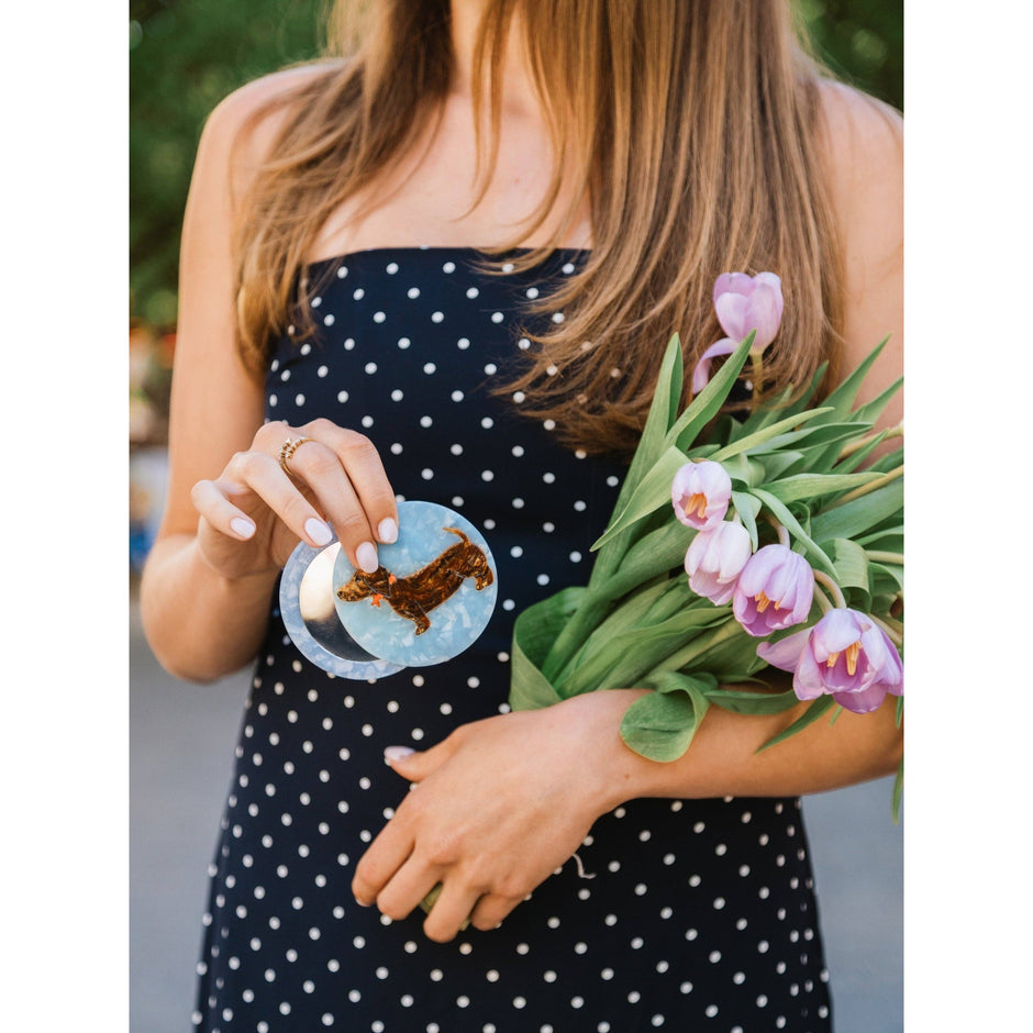 Woman holding hand-painted dachshund compact mirror with pink tulips in black polka dot dress
