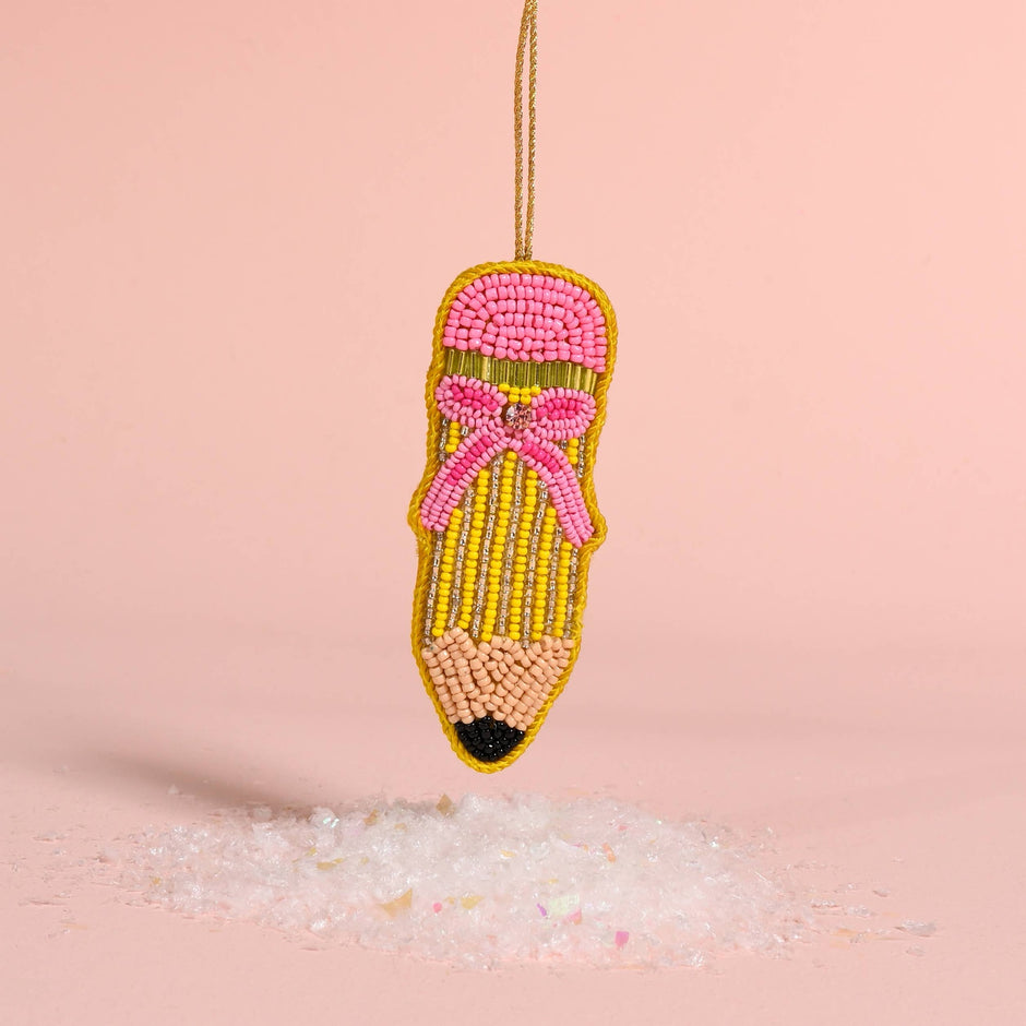 Handcrafted beaded pencil ornament with pink and gold beadwork hanging against pink background