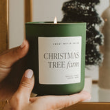 Sweet Water Decor Christmas Tree Farm soy candle held in hand with festive holiday decor background