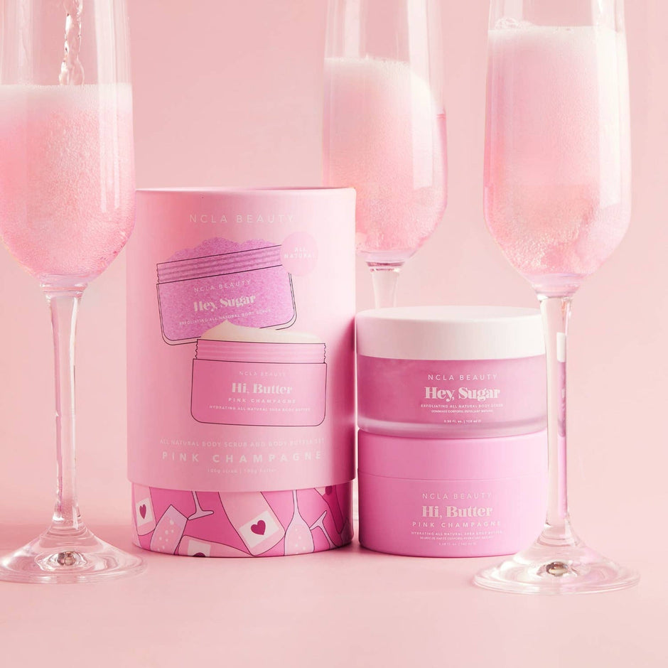 NCLA Beauty Pink Champagne body care set with scrub and butter displayed with champagne glasses