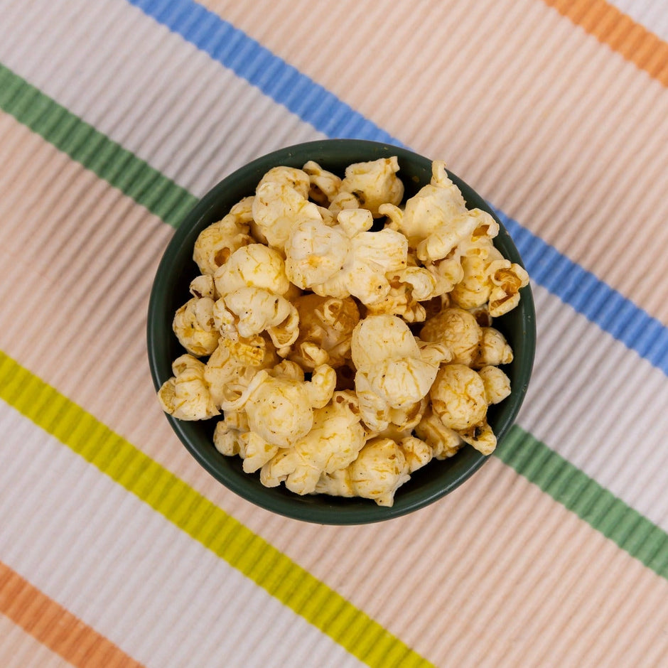 Poppy hand-crafted popcorn with caramelized onion and sage in black bowl on colorful striped background