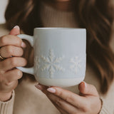 Woman holding white stoneware coffee mug with embossed snowflake design for Christmas