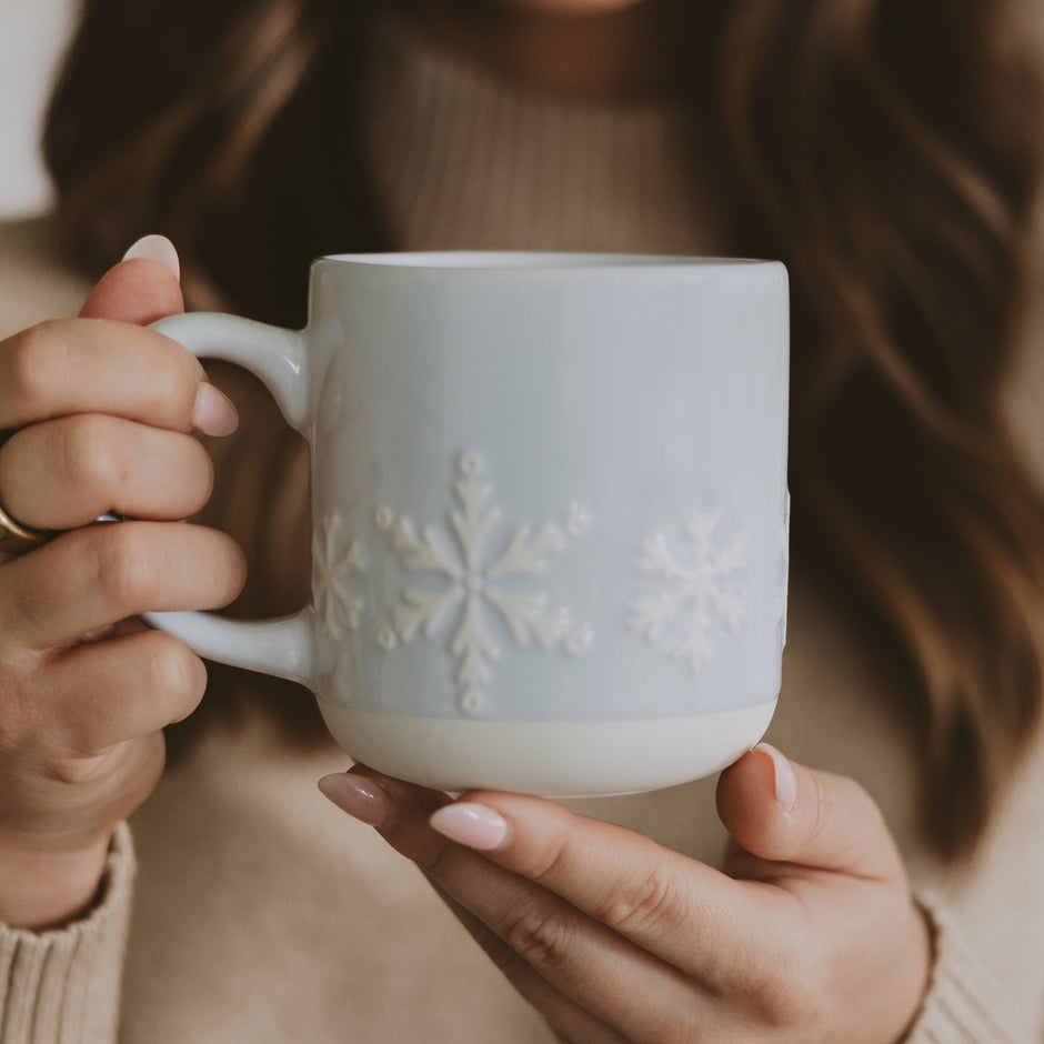Woman holding white stoneware coffee mug with embossed snowflake design for Christmas
