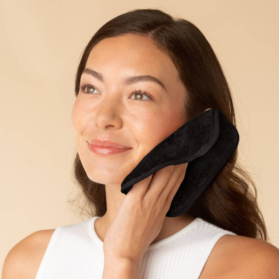 Woman using black microfiber face towel on cheek against neutral background