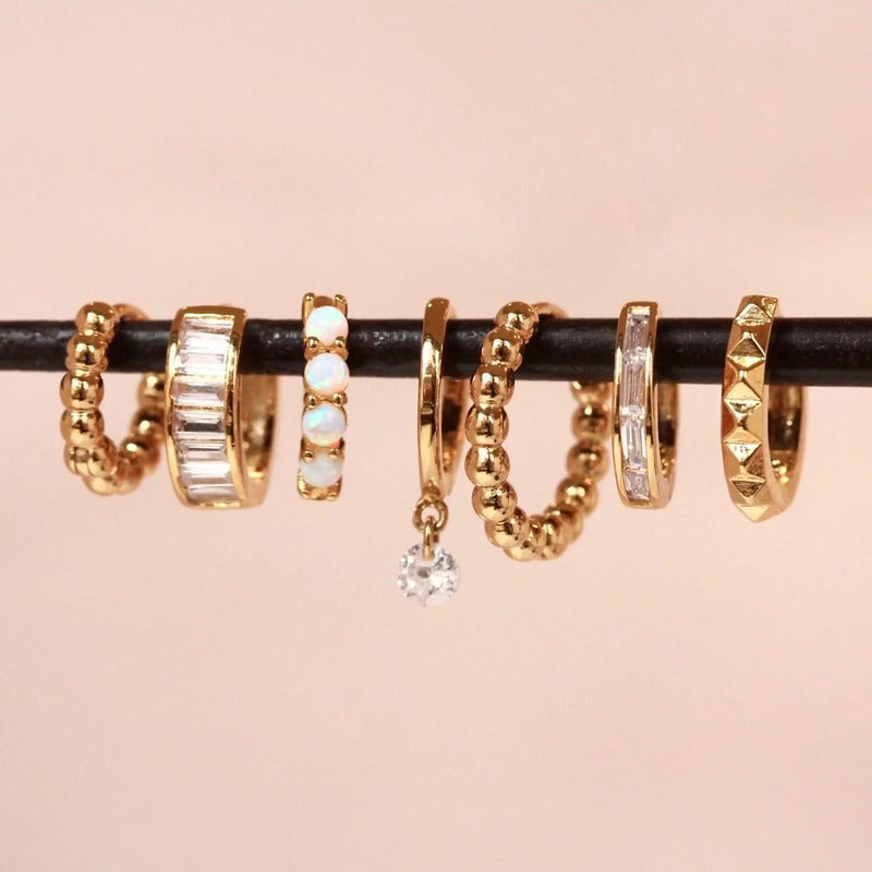 Gold mini baguette huggies earrings with crystals displayed on black rod against pink background